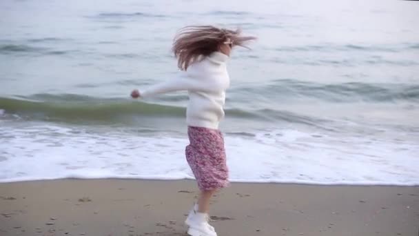 En stilren kvinna som virvlar glatt på höstens strand och sprider händerna — Stockvideo