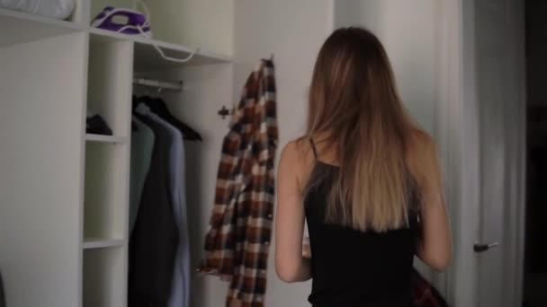 Blonde Frau wählt Outfit aus Kleiderschrank, zieht kariertes Hemd an — Stockvideo