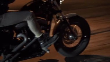 Gece şehir caddesinde motosikletini sürat yapan, tekerlekleri yakın vahşi bir adamın yan görüntüsü.