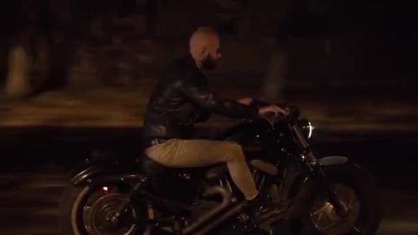 Vista lateral de un motorista en chaqueta de cuero montar en moto por la noche calle de la ciudad — Vídeos de Stock
