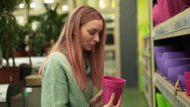 Kvinna väljer färgglada kruka för hem växter från hyllor i en blomsteraffär — Stockvideo