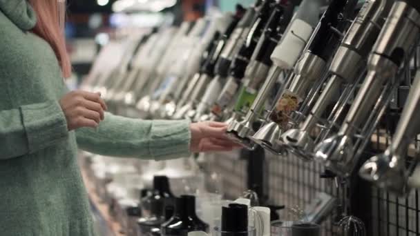 Kvinna väljer en mixer pinne genom att titta i apparaten butiken — Stockvideo