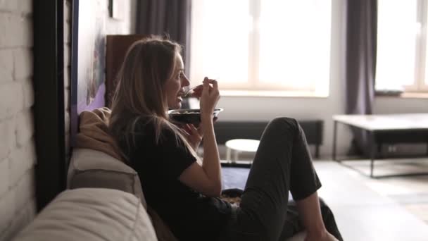 건강 한 젊은 여성, 편안하고 편안 해 보이는 죽 그릇을 들고 소파에 앉아 — 비디오