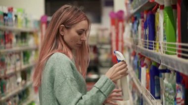 Sarışın kadın süpermarkette ev ürünleri etiketi okuyor.