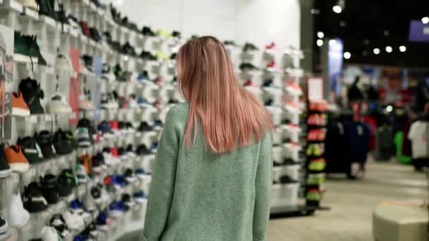 Покупая в магазине спортивной обуви, женщина ищет продавцов — стоковое видео