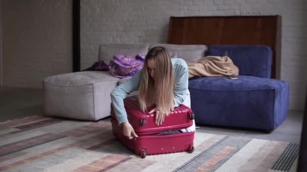 Женщина закрывает и застегивает молнию чемодан, готовится к поездке, готовит багаж к отпуску — стоковое видео