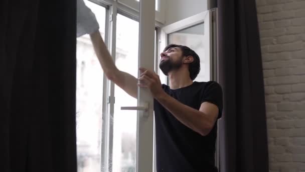 El hombre está limpiando la ventana, limpia la superficie, utiliza un trapo, de pie en un apartamento moderno — Vídeos de Stock