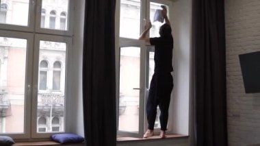 Adam yüksek pencereyi temizliyor, yüzeyi temizliyor, pencere kenarında duran bir bez parçası kullanıyor.