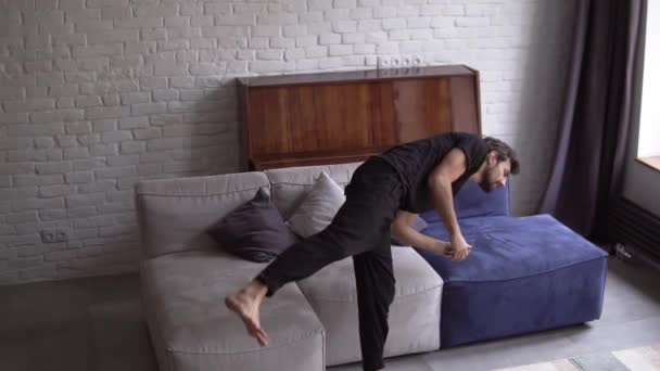 Fröhlicher Mann springt aufs Sofa, schaltet daheim im Wohnzimmer den Fernseher ein — Stockvideo