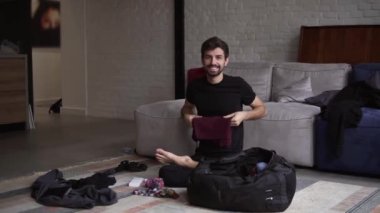 Oturma odasında seyahat etmek için sırtını toplayan gülümseyen bir adamın portresi.