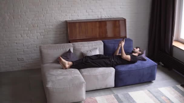 Homem deitado no sofá usando smartphone, rolando vários gestos como deslizar e rolar — Vídeo de Stock