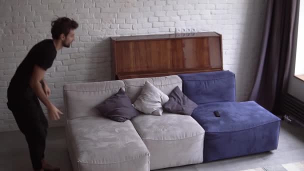 Ευτυχισμένος άνθρωπος πηδάει στον καναπέ, ανοίγει την τηλεόραση στο σπίτι στο σαλόνι — Αρχείο Βίντεο