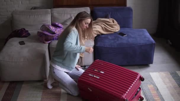 Woman closing and zipping suitcase, getting ready for road trip preparing luggage for vacation in a living room — Stock Video