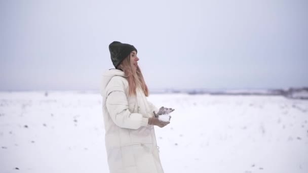 Playful young woman outdoor enjoying first snow, throwing a snowball to friends back — Stock Video