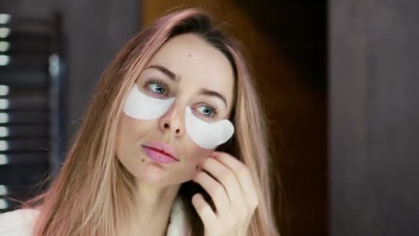 ブロンド女性でバスローブでホワイト目のパッチを削除しながらミラーを見て — ストック動画