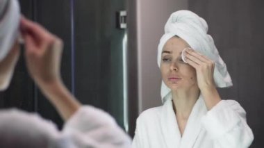 Genç bir kadın toner kullanıyor, tek kullanımlık pamuk kullanıyor, duştan sonra cilt bakımı yapıyor.