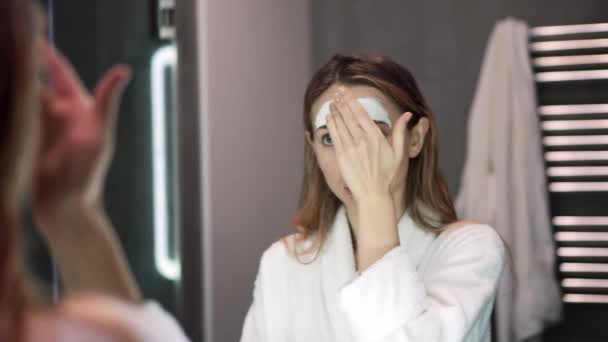 指で保湿のための白いマスクを入れたバスローブの女性の肖像 — ストック動画