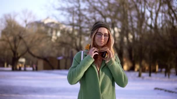 Attrayant fille marcher dans le parc d'hiver, écouter de la musique au téléphone, look élégant — Video