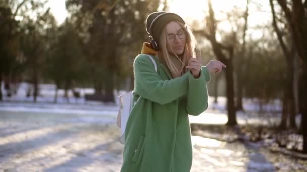 Ung kvinna dansa frikostigt i vinterparken, lyssna på musik på telefonen med hörlurar — Stockvideo