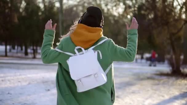 快乐的女人在冬天的公园里跳舞，用耳机听音乐，转来转去 — 图库视频影像