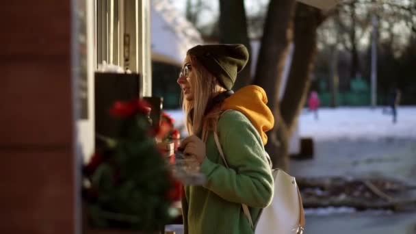 Mujer eligiendo mercancías en kiosco de la calle en el paseo de invierno. Sonriendo a la cámara — Vídeo de stock