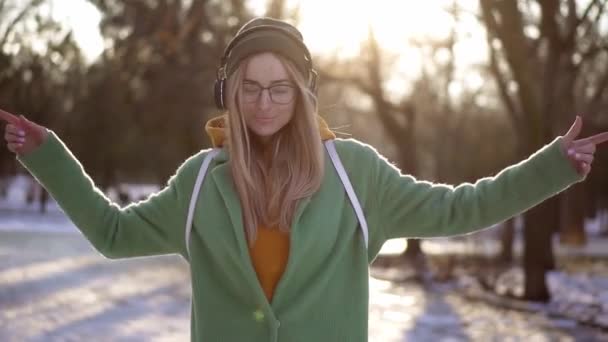 Piękna kobieta spaceruje i tańczy w zimowym parku, słuchając muzyki przez telefon za pomocą słuchawek — Wideo stockowe