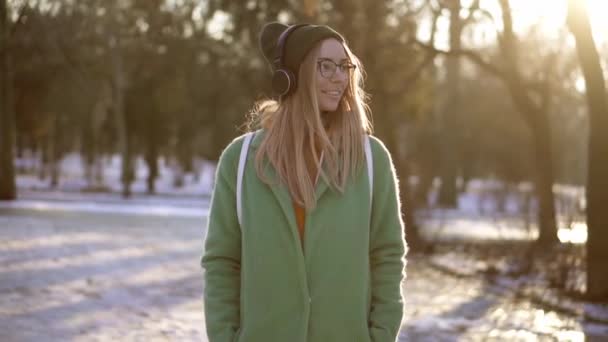 Chica despreocupada caminar en el parque de invierno, escuchando música en el teléfono de buen humor — Vídeo de stock