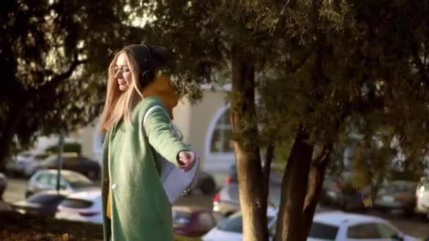 Mulher loira dança no parque de inverno, ouvindo música no telefone usando fones de ouvido, girando ao redor — Vídeo de Stock