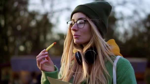 Blondýny dívka jíst hranolky venku na zimní ulici dip v kečupu — Stock video