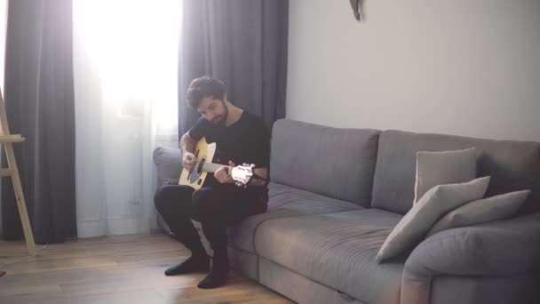 Potret seorang pria dengan gitar di tangannya di sofa — Stok Video