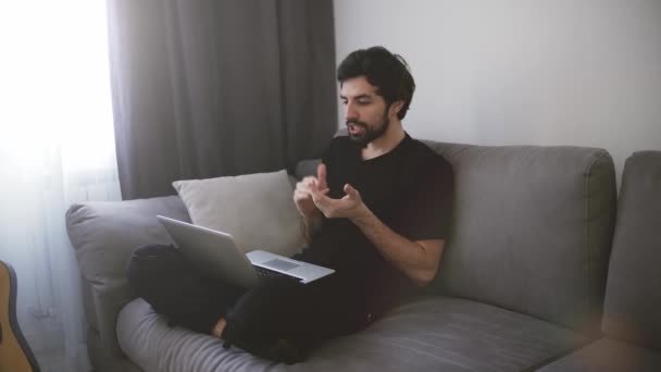 Hombre sentado en el sofá y haciendo una videollamada, haciendo un gesto — Vídeos de Stock