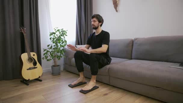 Férfi a nappaliban készül állni a körmök mezítláb a kanapéról — Stock videók