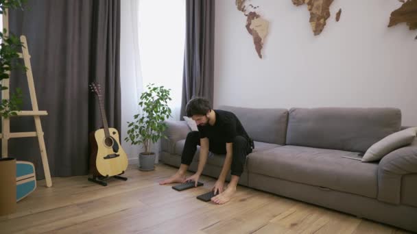 Pria di ruang tamu bersiap untuk berdiri di atas paku tanpa alas kaki dari sofa, gerakan lambat — Stok Video