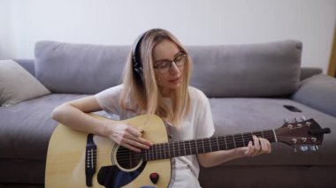 Kadın evinde gitar çalıyor, gitar çalarak ve şarkı söyleyerek mutlu oluyor.