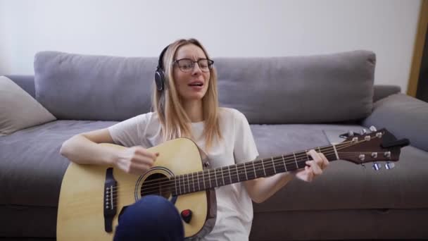 Mulher em fones de ouvido toca guitarra em sua casa, feliz se divertindo tocando guitarra e cantando — Vídeo de Stock