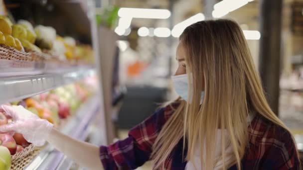 Mujer en guante y máscara recoge frutas manzanas en cesta en el supermercado — Vídeos de Stock