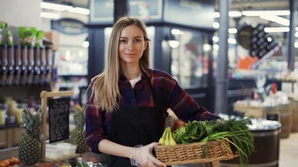 검은 앞치마를 입고 슈퍼마켓에서 과일과 야채가 가득 담긴 상자를 들고 있는 여성 슈퍼마켓 직원 — 비디오