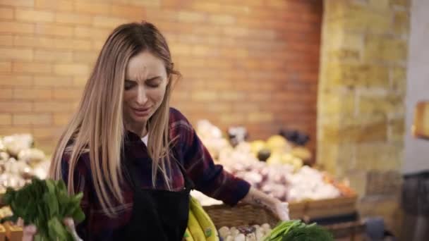 Uśmiechnięty pracownik w czarnym fartuchu aranżujący zieleninę w supermarkecie, bawiący się podczas pracy — Wideo stockowe
