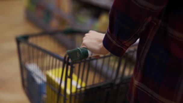 Las manos femeninas llevan un carro en el supermercado a través de pasillos — Vídeo de stock