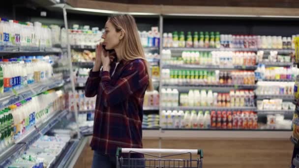 Frau kauft im Supermarkt ein und telefoniert mit Handy — Stockvideo