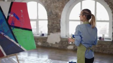 Kadın geniş fırça ve renk kullanıyor. Resim stüdyosundaki tuvale sıçrayan jestler.