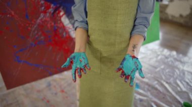 Resim yaparken ellerini gösteren bir kadının portresi, sanat eserlerinin yanında duran.