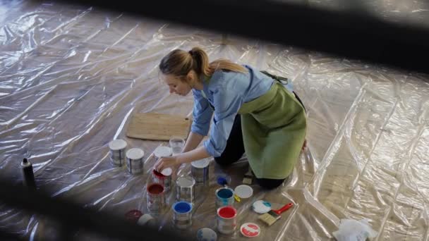 Mujer en el estudio abren diferentes colores de pintura en tarros de metal en el suelo en cámara lenta — Vídeos de Stock