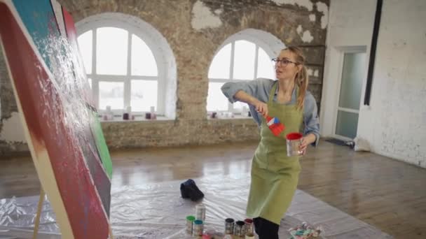 Женщина эмоционально создает шедевр абстрактной живописи в студии, разбрызгивает краски — стоковое видео