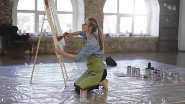 Γυναίκα καλλιτέχνης που εργάζεται με μεγάλο πινέλο και πλατύ καμβά στο εργαστήριο στέκεται στα γόνατα — Αρχείο Βίντεο