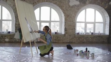 Atölyede büyük boya fırçası ve geniş tuval ile çalışan kadın sanatçı