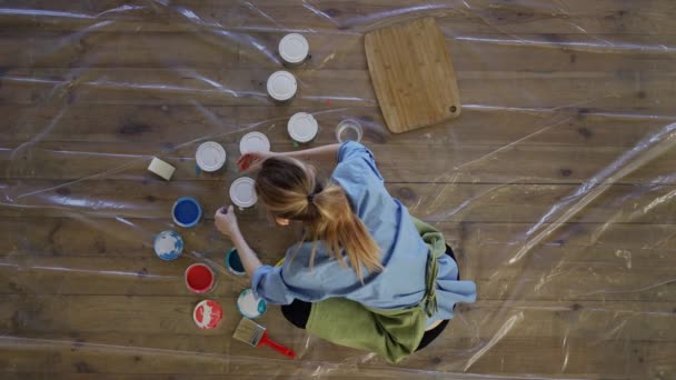 Mujer en el estudio abren diferentes colores de pintura en tarros de metal en el suelo, vista desde arriba — Vídeos de Stock