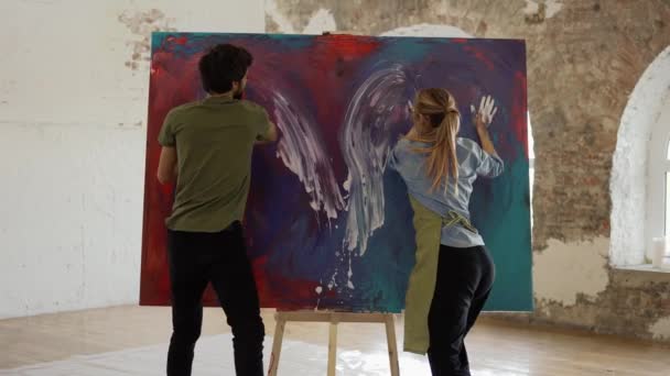 Страстная пара, держащая на холсте разноцветные краски, создает картину вместе — стоковое видео