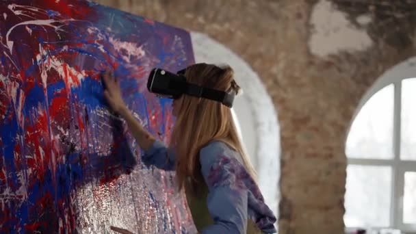 VRマスクの女はイーゼルの抽象画にペイントを塗る — ストック動画