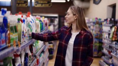 Mağazadaki bir ev eşyasında deterjanı seçen kadın, onu el arabasına koy.